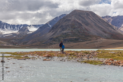 Father and son are walking along the grass near the mountain lake of the Mongolian Altai