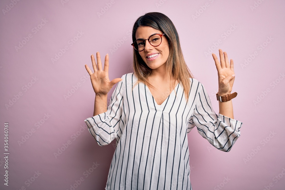 Young beautiful woman wearing casual striped t-shirt and glasses over pink background showing and pointing up with fingers number nine while smiling confident and happy. Young beautiful woman wearing casual striped t-shirt and glasses over pink background showing and pointing up with fingers number nine while smiling confident and happy.