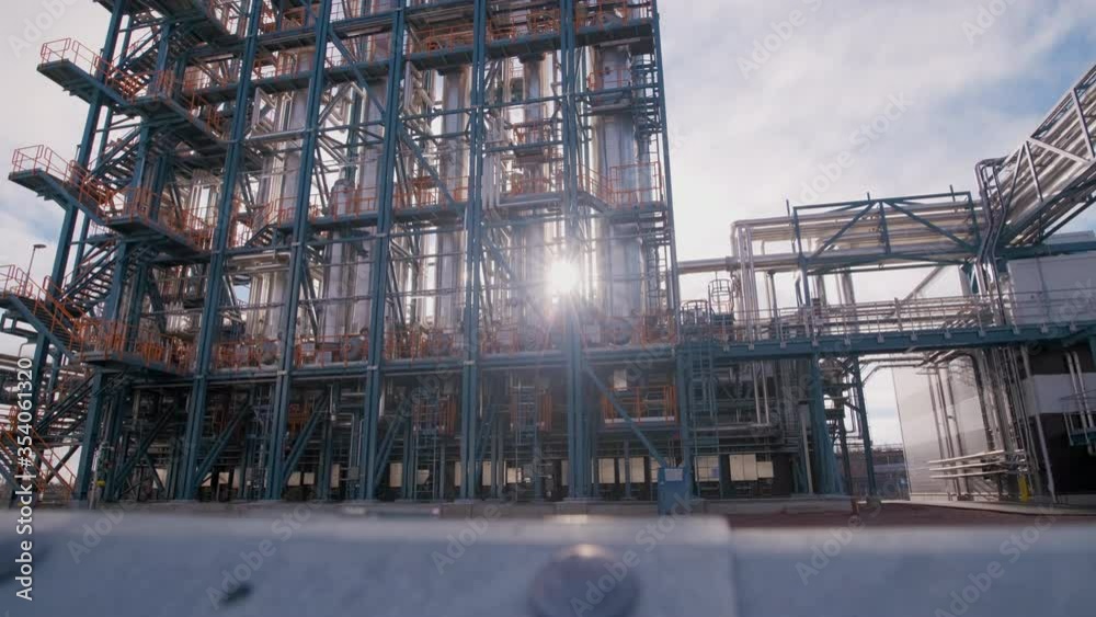 Wide shot of a grey modern newly built industry building. Camera dolly pans from right to left. The warm sun behind the building reveals itself through the metal pillars. 4K UHD slowmotion. Wide shot of a grey modern newly built industry building. Camera dolly pans from right to left. The warm sun behind the building reveals itself through the metal pillars. 4K UHD slowmotion.