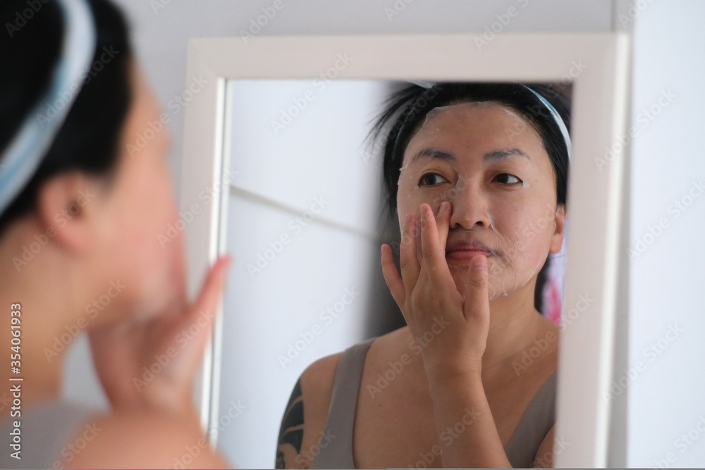 close up one young Asian woman doing facial mask in the mirror at home close up one young Asian woman doing facial mask in the mirror at home