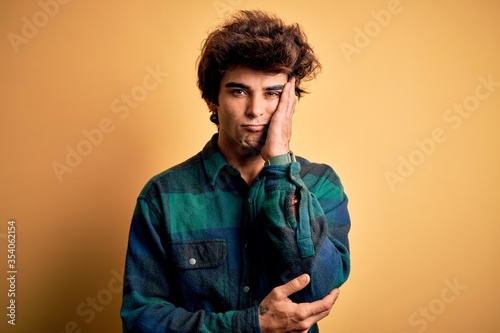 Young handsome man wearing casual shirt standing over isolated yellow background thinking looking tired and bored with depression problems with crossed arms. © Krakenimages.com