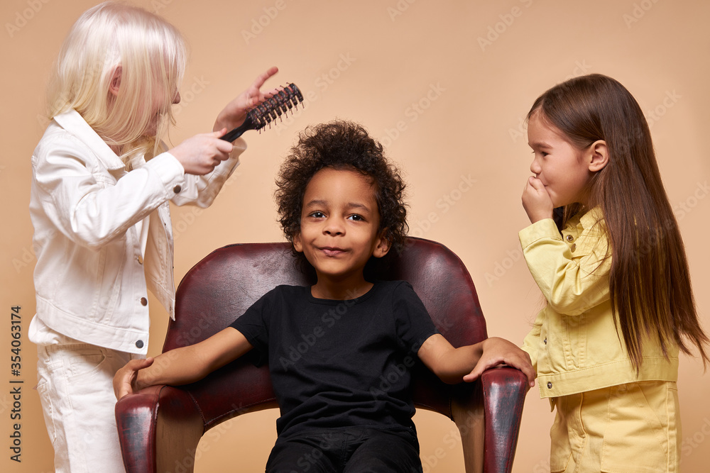 portrait of friendly diverse kids playing hairdressers. two girls comb boy's curly hair, happy smiling children with unusual diverse appearance. natural beauty