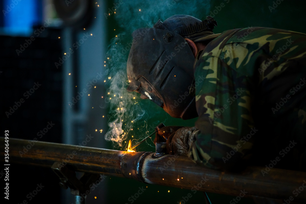 Welder at work. Man in a protective mask. The welder makes seams on the metal. Sparks and smoke when welding.