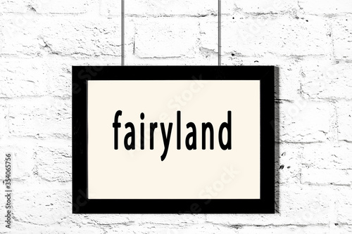 Obraz na plátně Black frame hanging on white brick wall with inscription fairyland
