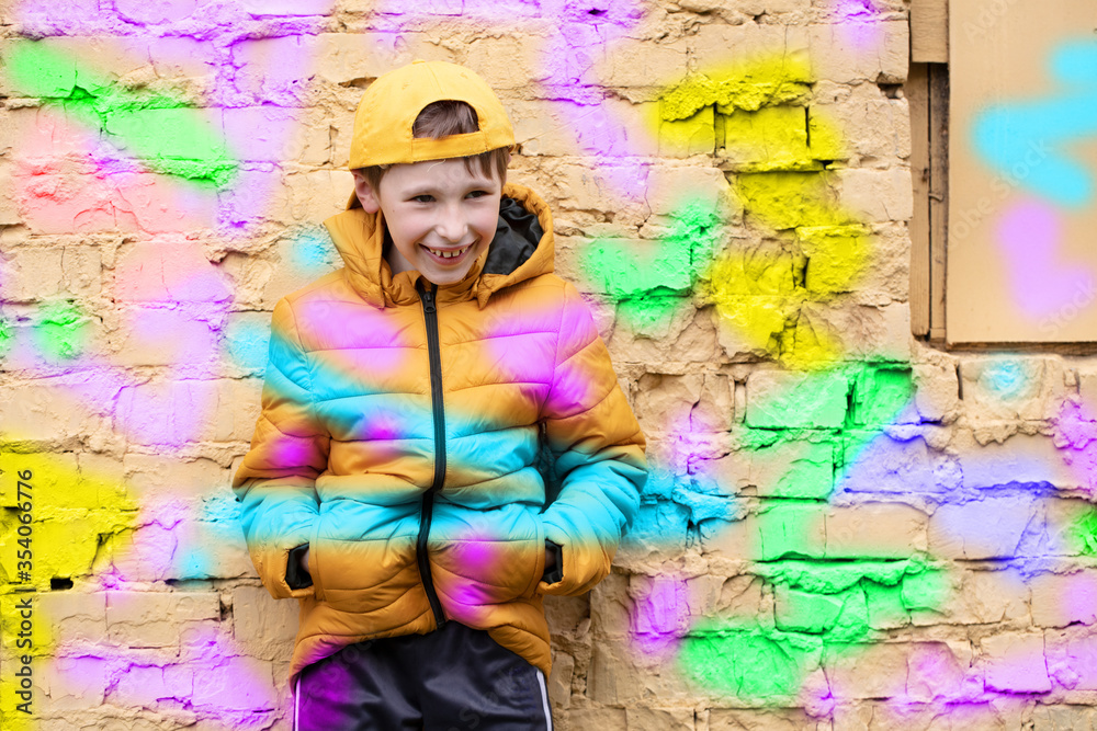Obraz premium Child in graffiti. The boy is standing against a brick wall in fashionable clothes and a baseball cap, outlined with bright colors.