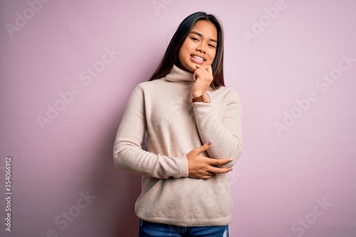 Young beautiful asian girl wearing casual turtleneck sweater over isolated pink background looking confident at the camera with smile with crossed arms and hand raised on chin. Thinking positive.