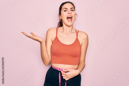 Young beautiful fitness woman wearing sport excersie clothes using measuring tape very happy and excited, winner expression celebrating victory screaming with big smile and raised hands © Krakenimages.com