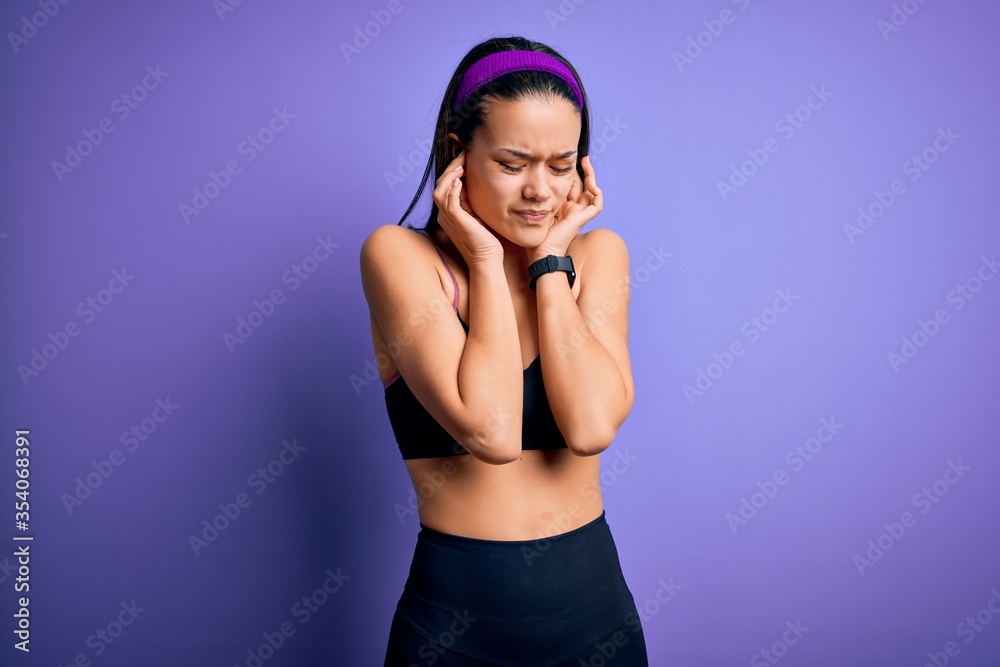 Obraz premium Young beautiful sporty girl doing sport wearing sportswear over isolated purple background covering ears with fingers with annoyed expression for the noise of loud music. Deaf concept.