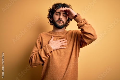 Young handsome man with beard wearing casual sweater standing over yellow background Touching forehead for illness and fever, flu and cold, virus sick
