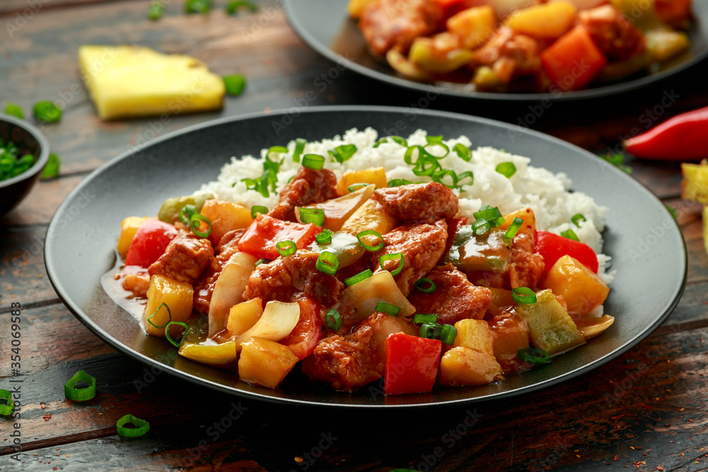 Pineapple and Chicken in sweet and sour sauce with bell pepper, rice and spring onion in black plate Pineapple and Chicken in sweet and sour sauce with bell pepper, rice and spring onion in black plate