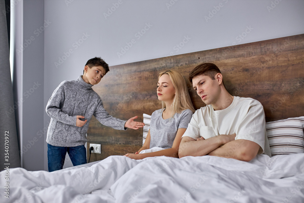 little child ask parents to stop quarreling, offended parents lie on bed don't talking with each other, son try to reconcile them