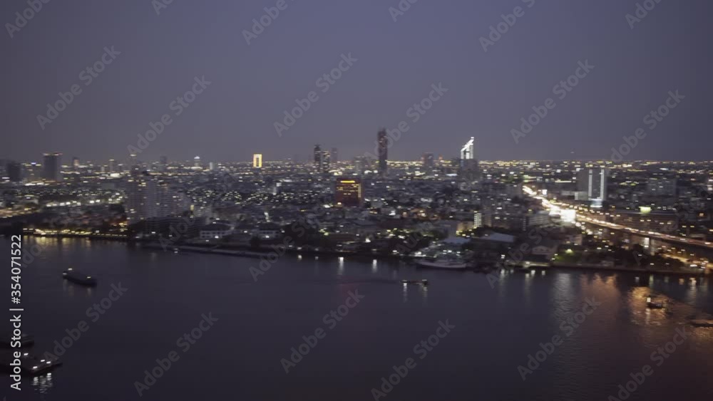 Panning shot of river by illuminated buildings in modern city against sky at night - Bangkok, Thailand Panning shot of river by illuminated buildings in modern city against sky at night - Bangkok, Thailand