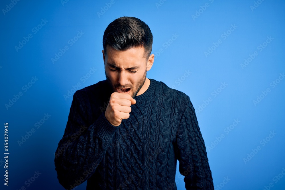Young handsome man wearing casual sweater standing over isolated blue background feeling unwell and coughing as symptom for cold or bronchitis. Health care concept.