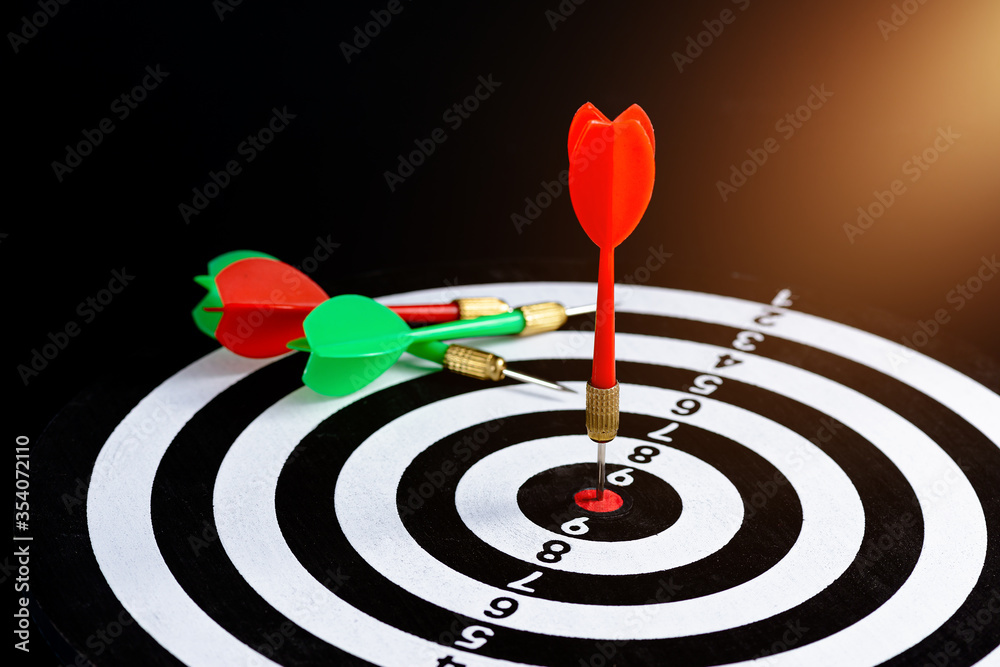 Red and green dart arrow hitting target center is Dart board Isolated on black background Red and green dart arrow hitting target center is Dart board Isolated on black background