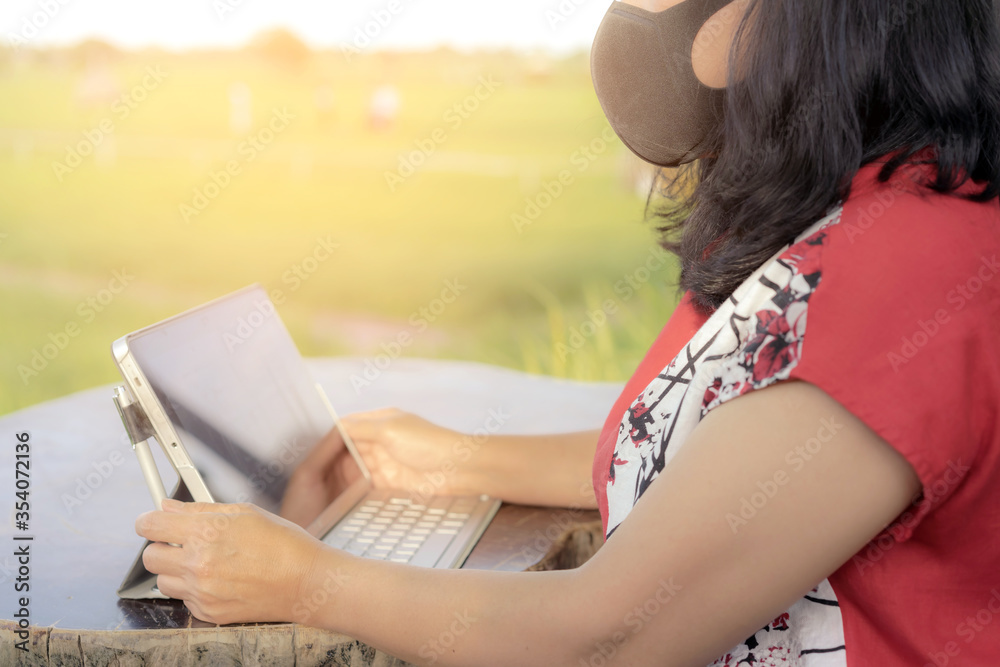 A quarantine woman wear a protective mask to prevent the spread of  of the Corona virus (Covid-19) ,Use a laptop to work from home in the rice field. New normal concept.Selective focus