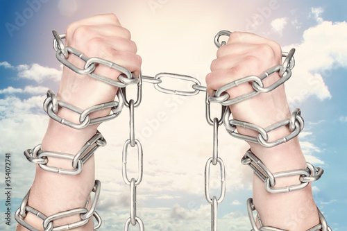 Two hands shackled a metal chain on blue sky background. Freedom concept