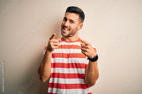 Young handsome man wearing casual striped t-shirt standing over isolated white background pointing fingers to camera with happy and funny face. Good energy and vibes.