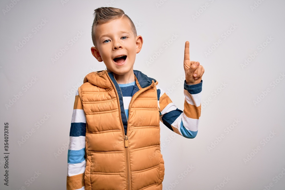 Young little caucasian kid with blue eyes standing wearing winter coat over isolated background pointing finger up with successful idea. Exited and happy. Number one. Young little caucasian kid with blue eyes standing wearing winter coat over isolated background pointing finger up with successful idea. Exited and happy. Number one.