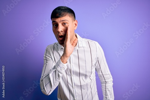 Young handsome hispanic man wearing elegant business shirt standing over purple background hand on mouth telling secret rumor, whispering malicious talk conversation