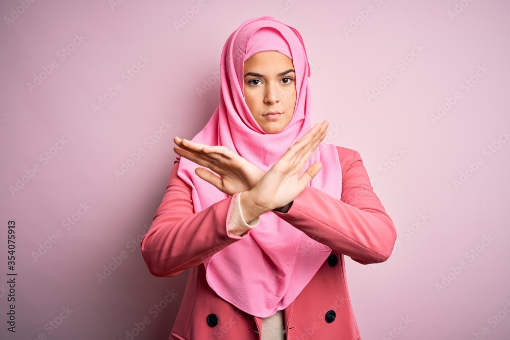 Young beautiful girl wearing muslim hijab standing over isolated pink background Rejection expression crossing arms and palms doing negative sign, angry face Young beautiful girl wearing muslim hijab standing over isolated pink background Rejection expression crossing arms and palms doing negative sign, angry face