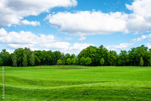 Empty golf course with trees in the background and blue sky with clouds..