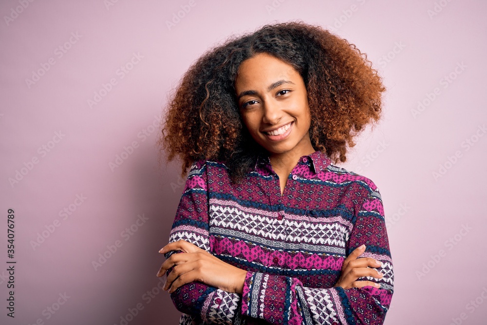 Young african american woman with afro hair wearing colorful shirt over pink background happy face smiling with crossed arms looking at the camera. Positive person. Young african american woman with afro hair wearing colorful shirt over pink background happy face smiling with crossed arms looking at the camera. Positive person.