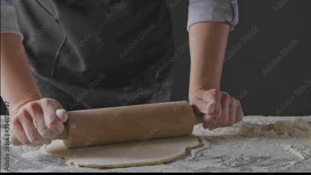 Female hands are rolling fresh dough on the table with the help of a rolling pin. Fresh flour is scattered around. Slow motion, Full HD video, 240fps, 1080p. Female hands are rolling fresh dough on the table with the help of a rolling pin. Fresh flour is scattered around. Slow motion, Full HD video, 240fps, 1080p.