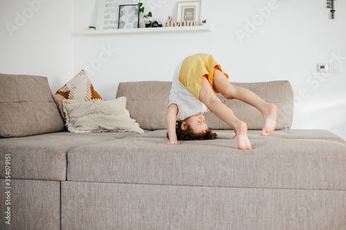 Cute little toddler girl tumbling on sofa at home. photo