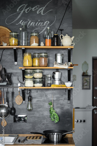 The interior of the kitchen in dark colors with shelves and a bunch of greens for tea. Storage jars  coffee maker  mugs  countertops.
