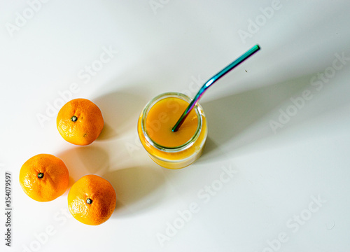 Photo of a delicious and healthy juice with a reusable straw and some mandarins nearby,
