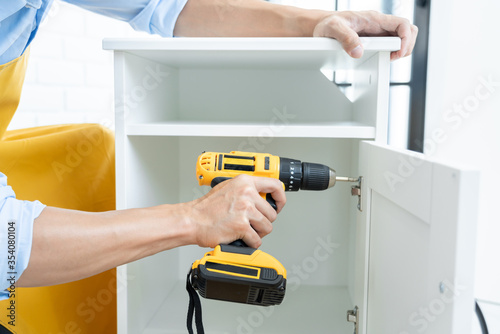 Close up portrait and details of caucasian male worker using electric screwdriver instrument in hand and repairing new wooden desk, home improvement concept. photo