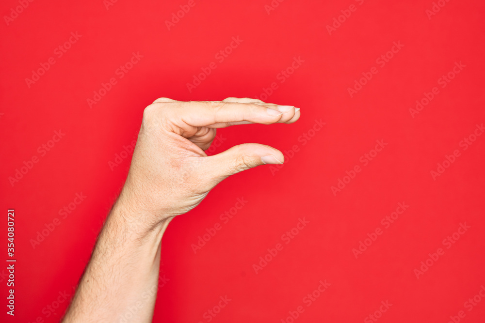 Hand of caucasian young man showing fingers over isolated red background picking and taking invisible thing, holding object with fingers showing space