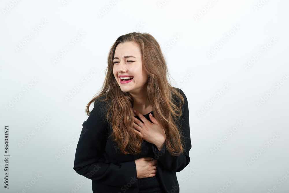 Young Attractive Woman Brunette In In Black T-Shirt And Sweater On White Background, Happy Female Smiling, Laughing, Holding Hand To Her Stomach. Joy Of The People In A Good Mood Young Attractive Woman Brunette In In Black T-Shirt And Sweater On White Background, Happy Female Smiling, Laughing, Holding Hand To Her Stomach. Joy Of The People In A Good Mood