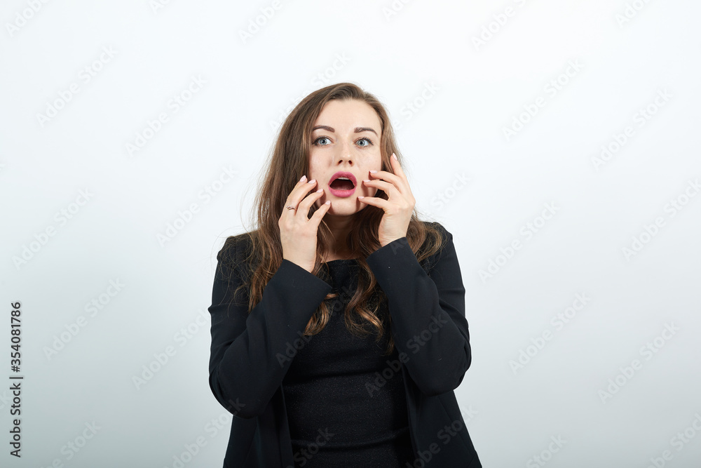 Young Attractive Woman Brunette In In Black T-Shirt Sweater On White Background, A Shocked Female Holds Hands To Her Face And Reacts Emotionally. Human Fear, Surprise Young Attractive Woman Brunette In In Black T-Shirt Sweater On White Background, A Shocked Female Holds Hands To Her Face And Reacts Emotionally. Human Fear, Surprise