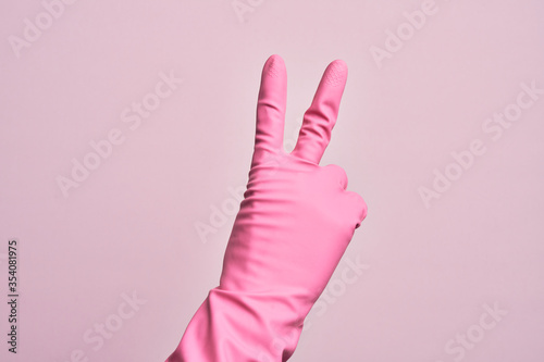 Hand of caucasian young man with cleaning glove over isolated pink background counting number 2 showing two fingers, gesturing victory and winner symbol