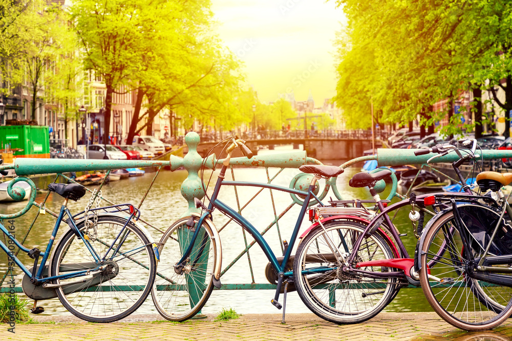 Bicycles on the bridge in Amsterdam, Netherlands against a canal and old buildings during summer sunny day. Amsterdam postcard iconic view. Tourism concept.