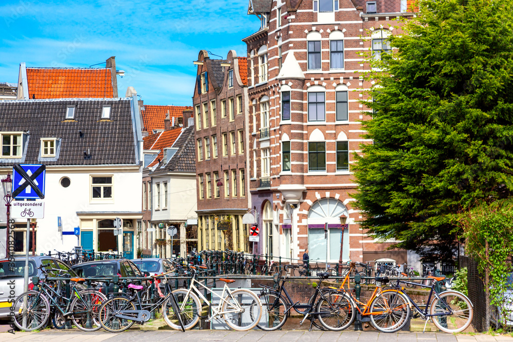 Old bicycles on the bridge in Amsterdam, Netherlands against a canal and old buildings during summer sunny day. Amsterdam postcard iconic view. Tourism concept.