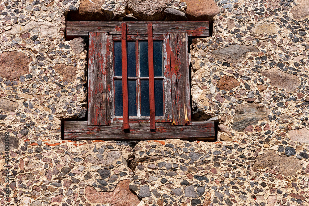 Window with wooden platband on the rough rural stone ancient wall background