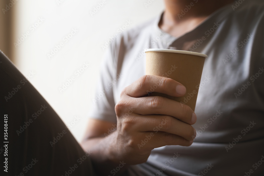 paper cup with coffee in hand at the man in the room with soft-focus and over light in the background paper cup with coffee in hand at the man in the room with soft-focus and over light in the background