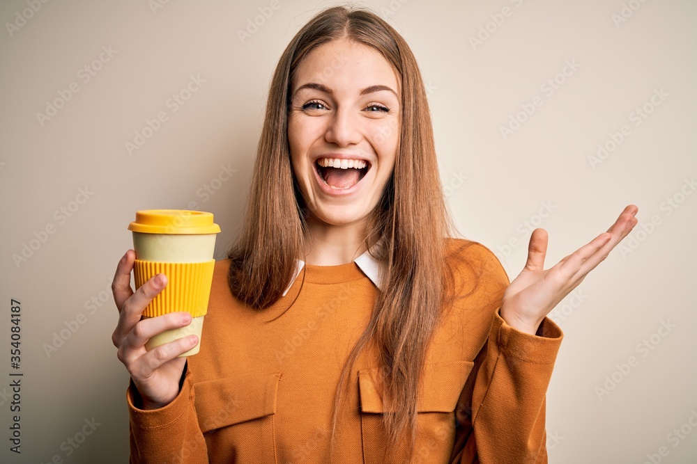 Young beautiful redhead woman drinking cup of coffee over isolated white background very happy and excited, winner expression celebrating victory screaming with big smile and raised hands Young beautiful redhead woman drinking cup of coffee over isolated white background very happy and excited, winner expression celebrating victory screaming with big smile and raised hands