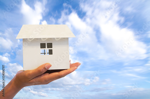 Close up Hand woman holding white house model isolate on blue sky background. Mortgage concept