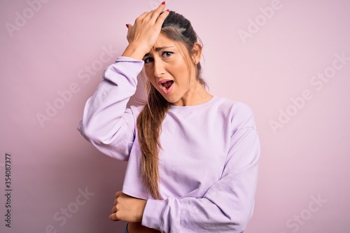 Young beautiful sport woman wearing sweatshirt over pink isolated background surprised with hand on head for mistake, remember error. Forgot, bad memory concept. © Krakenimages.com