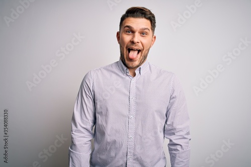 Young business man with blue eyes standing over isolated background sticking tongue out happy with funny expression. Emotion concept.