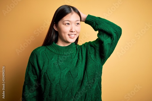 Young beautiful asian woman wearing green winter sweater over yellow isolated background smiling confident touching hair with hand up gesture, posing attractive and fashionable © Krakenimages.com