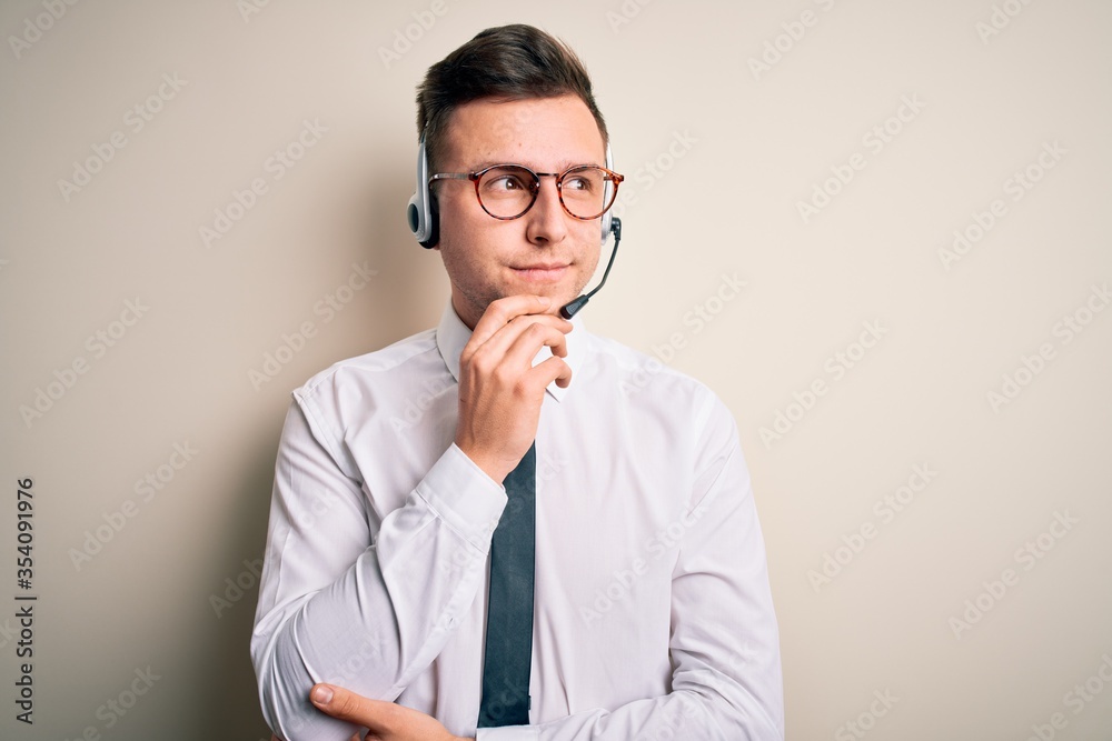 Young handsome caucasian business man wearing call center headset at customer service with hand on chin thinking about question, pensive expression. Smiling with thoughtful face. Doubt concept. Young handsome caucasian business man wearing call center headset at customer service with hand on chin thinking about question, pensive expression. Smiling with thoughtful face. Doubt concept.