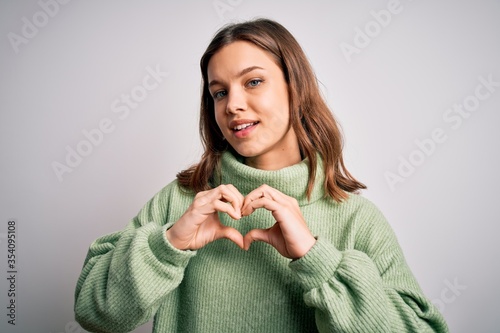 Young beautiful blonde girl wearing winter sweater standing over isolated background smiling in love showing heart symbol and shape with hands. Romantic concept.