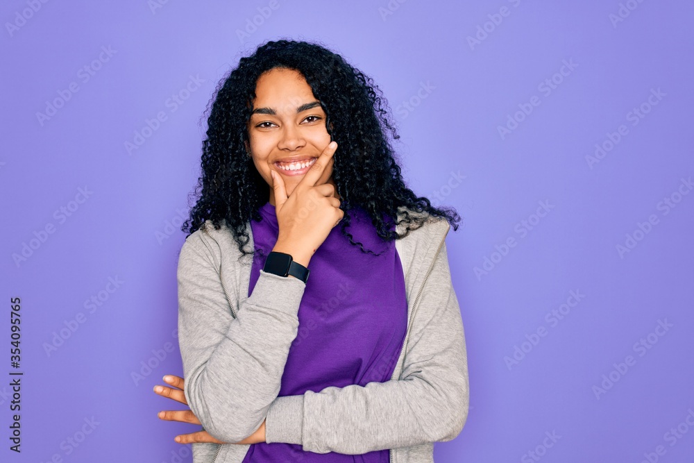 Young african american sporty woman wearing casual sweatshirt over purple background looking confident at the camera smiling with crossed arms and hand raised on chin. Thinking positive. Young african american sporty woman wearing casual sweatshirt over purple background looking confident at the camera smiling with crossed arms and hand raised on chin. Thinking positive.