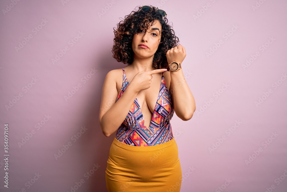 Young beautiful arab woman on vacation wearing swimsuit and sunglasses over pink background In hurry pointing to watch time, impatience, looking at the camera with relaxed expression Young beautiful arab woman on vacation wearing swimsuit and sunglasses over pink background In hurry pointing to watch time, impatience, looking at the camera with relaxed expression