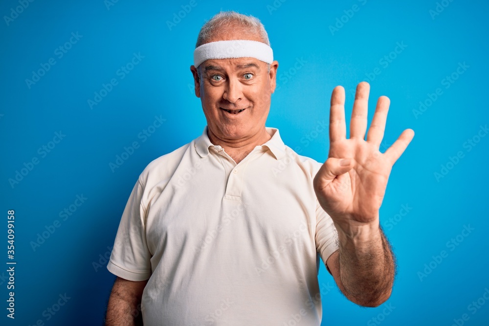 Naklejka premium Middle age hoary sportsman doing sport wearing sportswear over isolated blue background showing and pointing up with fingers number four while smiling confident and happy.