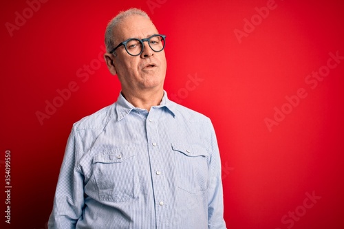 Middle age handsome hoary man wearing casual striped shirt and glasses over red background looking sleepy and tired, exhausted for fatigue and hangover, lazy eyes in the morning. © Krakenimages.com
